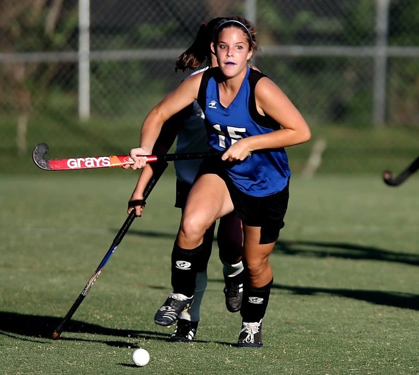 female player wearing custom blue field hockey uniform playing in green ground